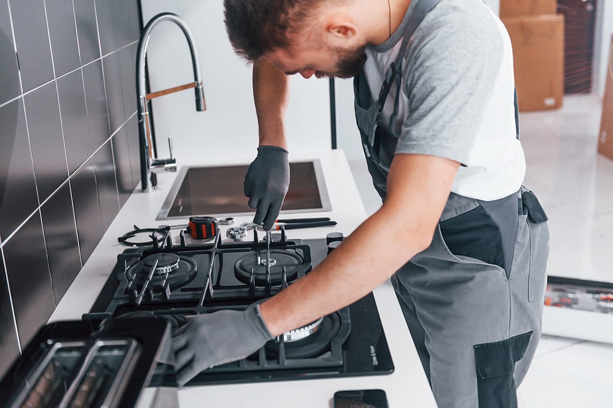 Young professional plumber in grey uniform working on the kitchen